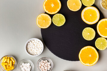 Various nutritional supplements, vitamins and minerals, pills and tablets, citrus fruits - lemon, orange and lime on black stone desk on grey background from above. Natural vitamins from fruits