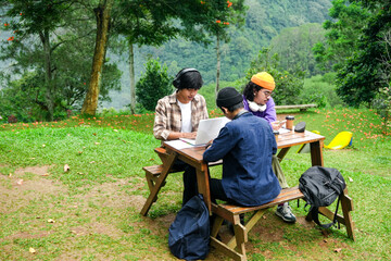 Young Students Collaborate Outdoors on Laptop Amidst Lush Greenery and Mountain Views