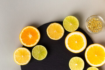 Various nutritional supplements, vitamins and minerals, pills and tablets, citrus fruits - lemon, orange and lime on black stone desk on grey background from above. Natural vitamins from fruits