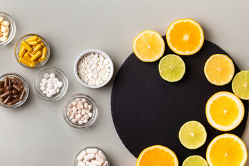 Various nutritional supplements, vitamins and minerals, pills and tablets, citrus fruits - lemon, orange and lime on black stone desk on grey background from above. Natural vitamins from fruits