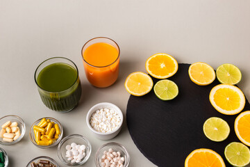 Nutritional supplements, various vitamins and minerals, pills from above on a black stone desk on green background. Smoothie, citrus fruits - lemon, orange and lime as a source of natural vitamins.