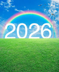 2026 white text with wind turbine on green grass field over rainbow, birds and blue sky with white clouds, Happy new year 2026 ecological cover concept
