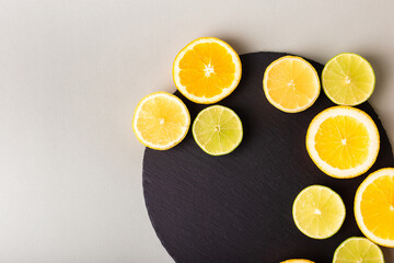 Citrus fruits - lemon, orange and lime on black stone desk on grey background from above. Healthy sweets. Natural vitamins from fruits