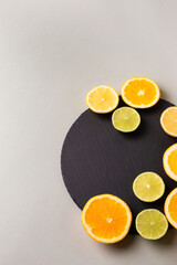 Citrus fruits - lemon, orange and lime on black stone desk on grey background from above. Healthy sweets. Natural vitamins from fruits