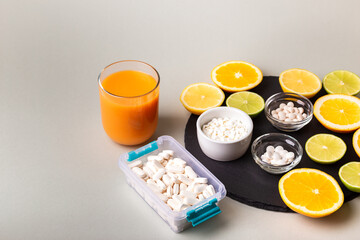 Nutritional supplements, various vitamins and minerals, pills from above on a black stone desk on green background. Smoothie, citrus fruits - lemon, orange and lime as a source of natural vitamins.