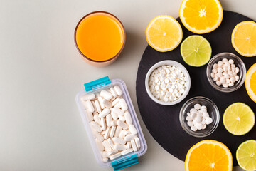 Nutritional supplements, various vitamins and minerals, pills from above on a black stone desk on green background. Smoothie, citrus fruits - lemon, orange and lime as a source of natural vitamins.