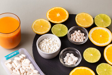 Nutritional supplements, various vitamins and minerals, pills from above on a black stone desk on green background. Smoothie, citrus fruits - lemon, orange and lime as a source of natural vitamins.