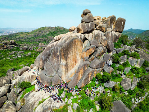 Aerial view of warm sunlight kissing the cool, gray rocks of Shere Hills, where tiny figures gather amidst the vibrant green landscape, Shere Hills, Plateau, Nigeria.