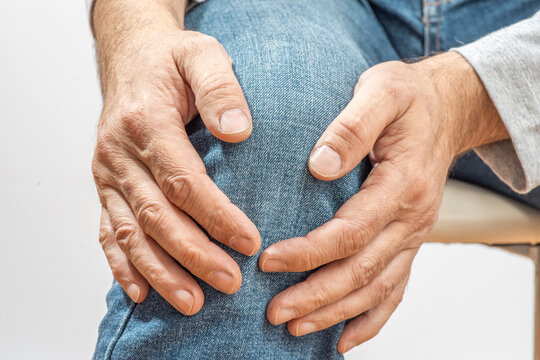 Arthritis symptoms, suffering from pain. The hands of the senior man massage a painful, inflamed male knee. Old age, health. Close up view..