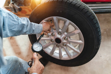 Man checking tire pressure with gauge on silver alloy wheel in garage during daylight, ensuring...