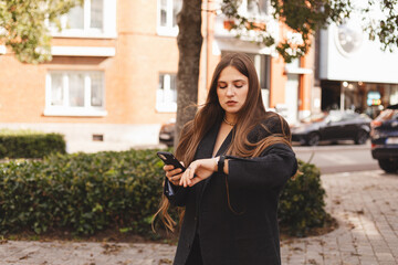Young woman concentrating while checking her smartwatch outdoors in a casual urban setting. Modern tech lifestyle, time management and daily routine captured in warm natural light and soft colors.