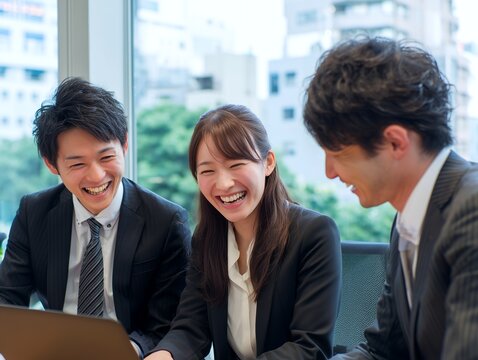 明るいオフィスで笑顔の日本人ビジネスチームが楽しく打ち合わせをする様子の写真