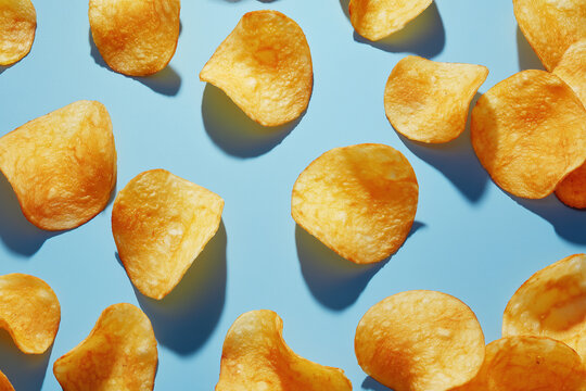 Golden potato chips scattered on a vibrant blue background, crispy snack close-up with appealing texture and shadow for food photography and advertising - Powered by Adobe