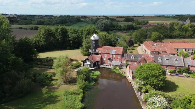 Ariel footage of Burnham Overy Staithe Mill in Norfolk England on the river Burn. Overy Water Mill, Windmill. Rural summer scene.