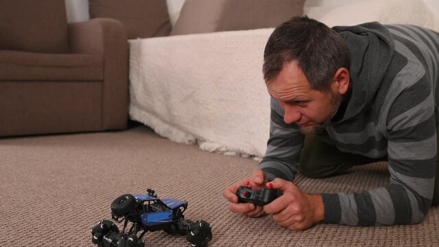 A bearded middle-aged man plays with a radio-controlled car at home with emotion.