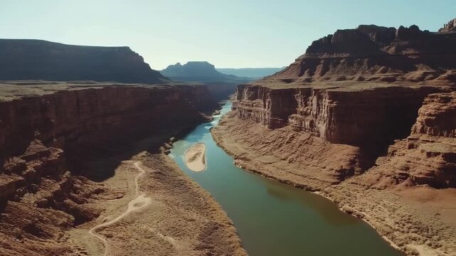 Aerial view of a river carving its way through a vast, sunlit red rock canyon