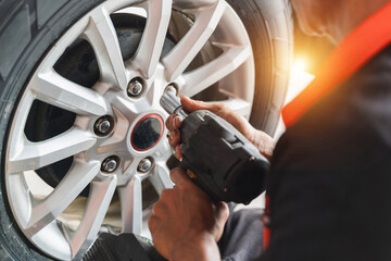 Mechanic Using Electric Tool to Tighten Lug Nuts on Silver Alloy Wheel During Car Maintenance in a Well-Lit Workshop Environment