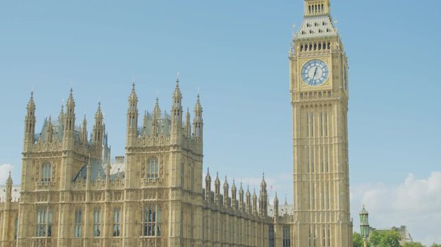 Close-up view of the Palace of Westminster and the Elizabeth Tower with the Big Ben clock face under a bright blue sky on a sunny day in London, England.