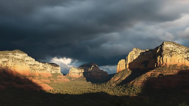 Sunlight illuminates red rock formations under a dark, dramatic stormy sky