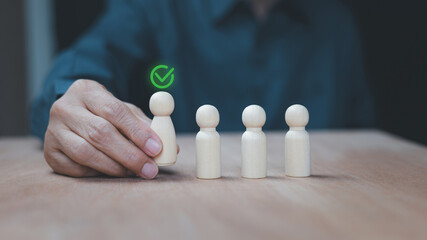 Selecting the best candidate from a group, a hand choosing a wooden figure with a green checkmark. Concept represents human resource management, recruitment, success, and talent acquisition.