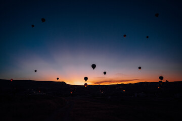 Goreme, Turkiye - 09 October 2019: View of hot air balloons floating serenely against the darkening sky as the last rays of sunset paint the horizon with hues of orange and blue.