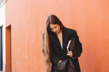 Elegant young long hair woman looking in her black leather bag her mobile phone or purse. Business...