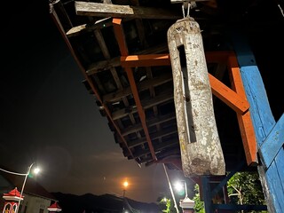 Close-up of a traditional bamboo kentongan hanging at night, symbolizing rural communication and Javanese cultural heritage.