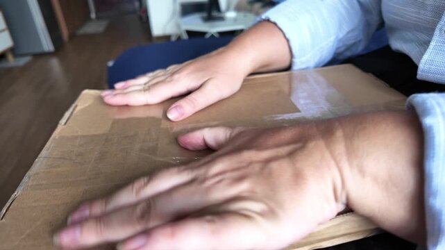 Close-up of a woman's hands taping a cardboard box with adhesive tape, side view