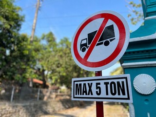 Road sign showing “Max 5 Ton” weight limit near a small town road with trees in the background.