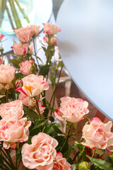 Close-up of light pink Spray Roses with picotee edges, arranged indoors near a table. The elegant bouquet creates a romantic atmosphere, with ample copy space for text or design elements.
