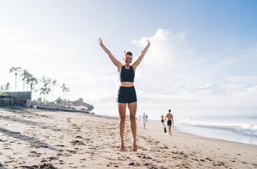 Young fit woman jumps with arms up, expressing freedom, digital detox, and joy from movement tracked by wearable tech in outdoor mindful routine.