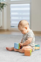 Baby girl sitting and playing with soft blocks on carpet. Developmental Milestones
