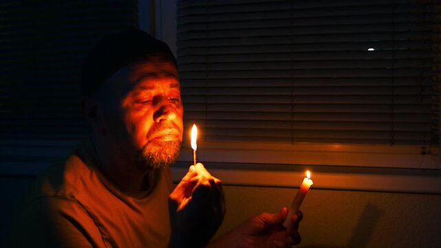 Blackout, No electricity. Man in a dark room near a window with candle. Depressed young man during a power outage.
