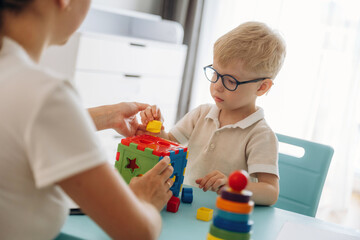Composes logic puzzles. Speech therapist is with young boy indoors