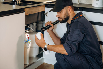 Plumber working in the kitchen under the sink