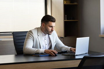 A focused young businessman works diligently at his desk, using a calculator and laptop in a modern...