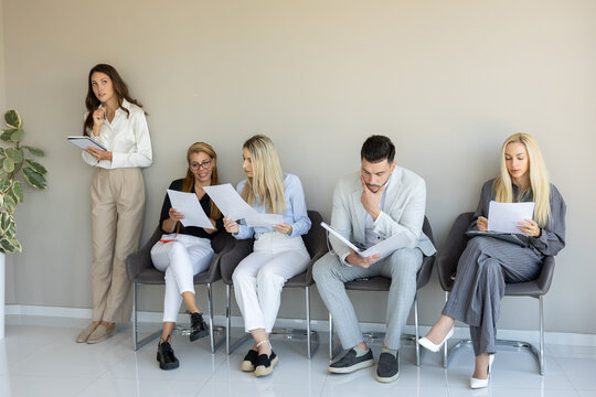 A group of professionals waits attentively in a modern office reception area, reviewing documents for an interview or meeting.