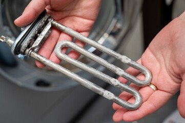 Hands holding washing machine heating element covered with limescale during appliance repair