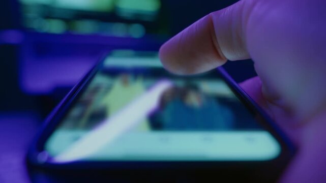 Close-up of a hand holds smartphone and scrolling through social media in dark room, symbolizing late-night doom scrolling and digital addiction habits. 