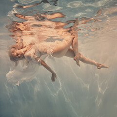 Woman with blonde hair in a lace white dress underwater