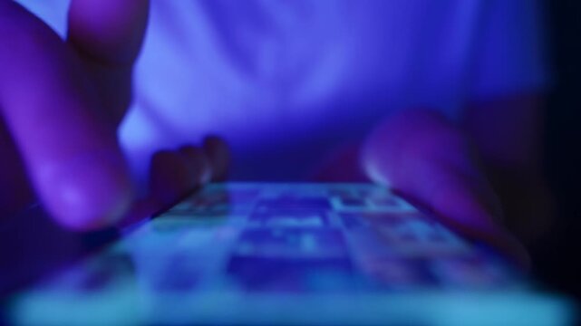 Close up of hands using a mobile phone in low light, browsing social networks and consuming endless online content. Doomscrolling and information overload.