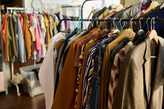 Clothing rack displaying assorted vintage garments hanging in thrift shop, various styles and fabrics visible, background showing additional racks filled with secondhand clothing