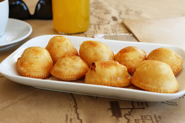 Close-up of traditional Greek kalitsounia pastries served on a white plate, drizzled with honey. Sweet cheese-filled fried pies typical of Cretan cuisine.