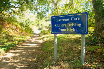 Warning of golfers at the tee seen on a rural country path which is about to exit near the golf tee at an English country club. The tee is just beyond the hedge on the right.