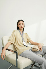 Elegant woman in a beige blouse with a striped scarf sitting comfortably indoors.