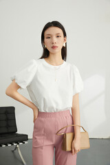 Young woman in white top and pink pants holding a handbag in a modern indoor setting.