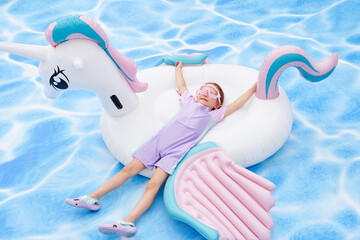 Joyful child relaxing on a unicorn float in a bright swimming pool.