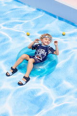 Boy enjoying summer fun in a blue inflatable ring by the pool.
