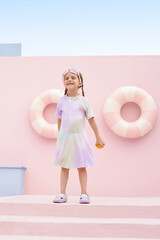 Joyful girl in a pastel dress standing outdoors with swimming rings.