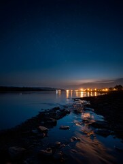 A serene night river reflects the soft glow of starlight and moonlight with distant city lights twinkling under a peaceful starry sky